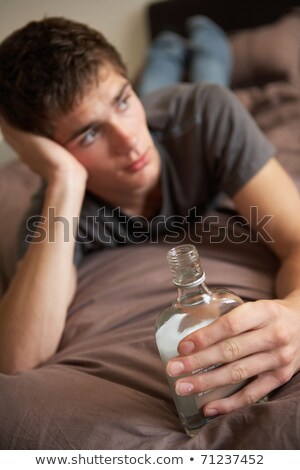 Foto d'archivio: Teenage Boy Lying In Bedroom Drinking