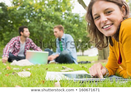 [[stock_photo]]: Female Student Using Tablet Pc While Lying On Grass
