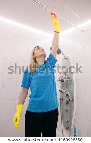 Imagine de stoc: Blonde Female Cleaning Pipe Under Ceiling In White Shower Cabin In Bathroom