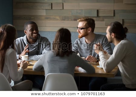 Foto stock: A Group Of Friends Sitting A Table And Talking Smiling While Ta