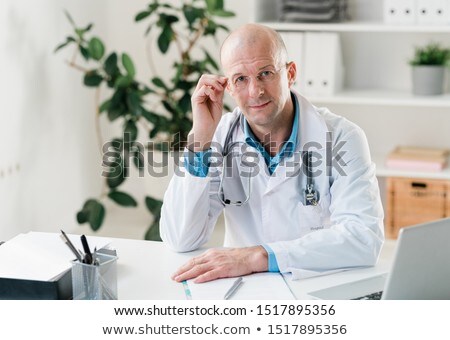 Zdjęcia stock: Serious Doctor In Whitecoat And Eyeglasses Looking At You By Workplace