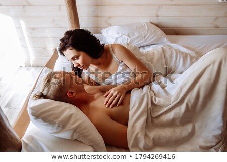 Foto d'archivio: Two Cheerful Woman Lying Together On Bed With White Sheets