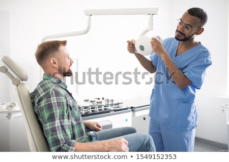 Сток-фото: Young Doctor In Uniform Holding Medical Equipment Or Lamp In Front Of Patient