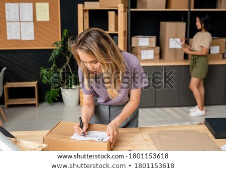 Stock photo: Young Female Manager Of Online Shop Writing Down Address Of Client On Top Of Box