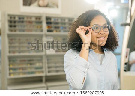 Stock fotó: Pretty Young Smiling Brunette Woman Trying On New Eyeglasses In Front Of Mirror