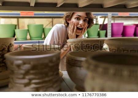 ストックフォト: Shocked Cute Woman Gardener Standing In Greenhouse Choosing Vase Pot For Plants