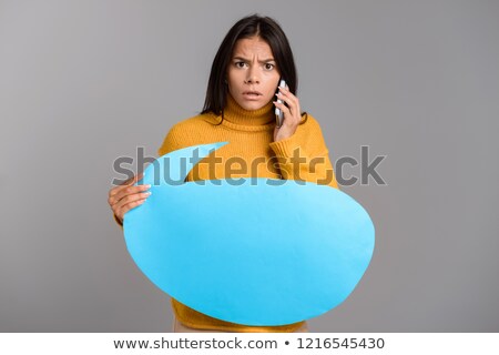 Foto stock: Confused Woman Posing Isolated Over Grey Wall Background Holding Speech Bubble Talking By Phone