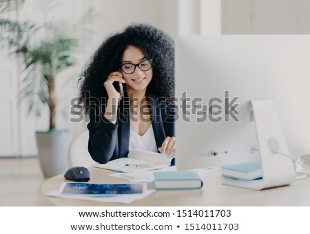 ストックフォト: Photo Of Satisfied Afro American Woman Calls Via Smartphone Makes Notes In Notepad Involved In Wor