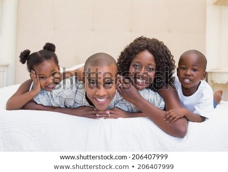 [[stock_photo]]: Front View Of Happy African American Family Relaxing On Bed And Looking At Camera In A Comfortable H