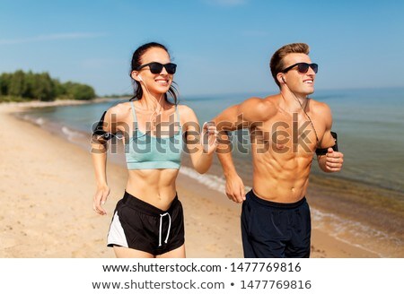 Foto stock: Couple With Earphones Running Along On Beach