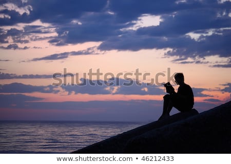 商業照片: 影傢伙坐在防波堤在傍晚時分在海邊讀