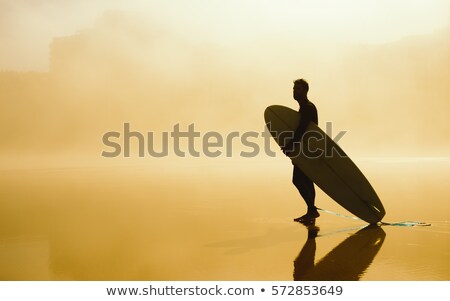 [[stock_photo]]: Surfer Holding His Surfboard On A Misty Urban Beach