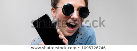 ストックフォト: Young Brunette Girl In Round Glasses Hairs Are Gathered In A Bun Girl With A Black Phone