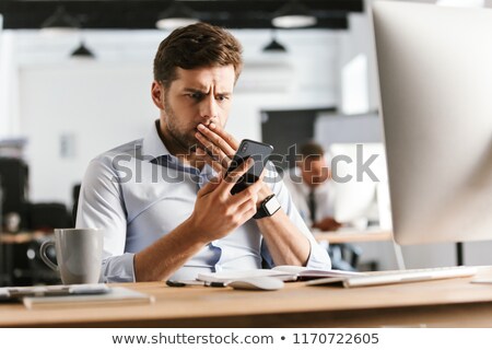 Stok fotoğraf: Shocked Business Man Using Smartphone And Covering His Mouth