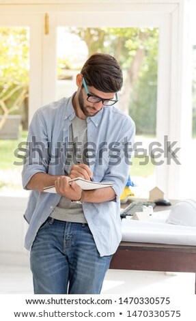Foto stock: A Young Man Is Standing Near A Table In The Office Holding A Pencil And A Glass Of Coffee A Young