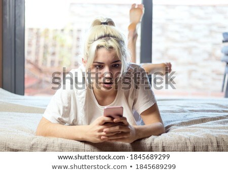 Adorable Smiling Blond Woman Lying In White Bed And Using A Smartphone Stockfoto © 2Design