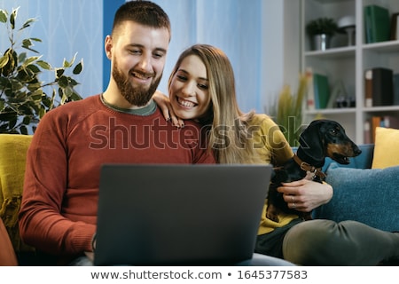 Foto stock: Couple Using Laptop With Their Pet Dog In Living Room At Home