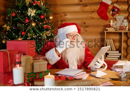 Foto stock: Serious Santa With Touchpad And Smartphone Making Online Order For Christmas