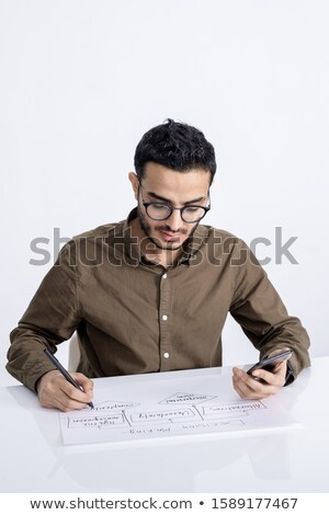 [[stock_photo]]: Young Confident Businessman With Smartphone And Pen Drawing Flow Chart On Paper