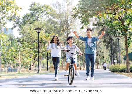 Stok fotoğraf: Parents Running With Their Child Riding Bicycle