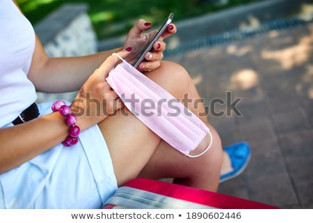 Foto stock: Unrecognizable Woman Sitting On The Bench And Pink Protective Mask In Her Hand