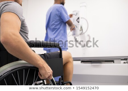 Stockfoto: Young Man With Sick Leg Sitting On Wheelchair In Front Of Medical Equipment