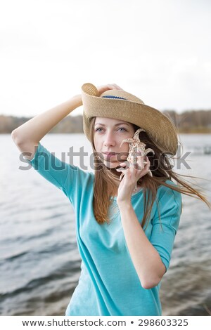 Foto stock: Freckled Girl In Hat Listening To Shell And Standing On Lake