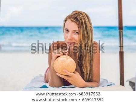 Foto stock: Young Woman Drinking Coconut Milk On Chaise Longue On Beach