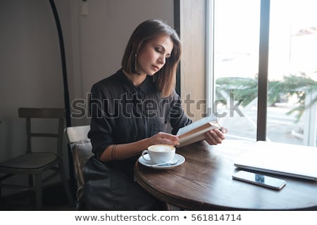 Stok fotoğraf: Woman Sitting At A Table Reading A Book And Dreams