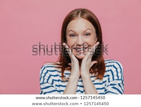 Stock photo: Portrait Of Cheerful Smiling Woman Touches Cheek Has Toothy Charming Smile Wears Shirt Looks At C