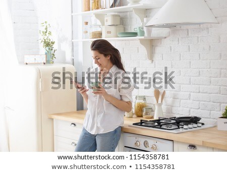 Stock photo: Beautiful Woman Using Cell Phone In Kitchen