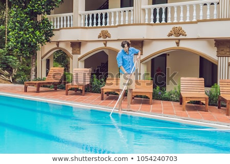 Stockfoto: Cleaner Of The Swimming Pool Man In A Blue Shirt With Cleaning Equipment For Swimming Pools Sunny