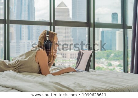 Foto stock: Young Woman Is Working On A Laptop In His Bed On A Background Of A Panoramic Window Overlooking The
