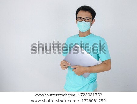Stock photo: Young Asian Man Wear Medical Mask Is Carrying A Laptop With Ok Hand Sign Indonesian Man Wearing Blu