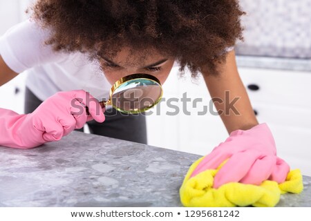 Foto stock: Woman Looking At Kitchen Counter With Magnifying Glass