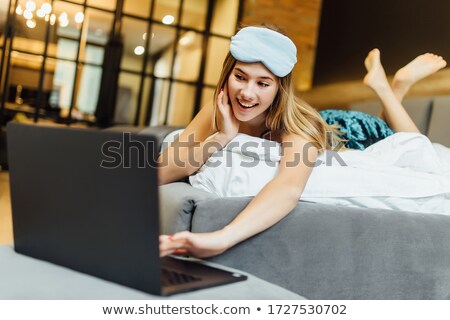 Foto stock: Young Blond Woman With Textile Mask On Face Lying On Bed In Front Of Laptop