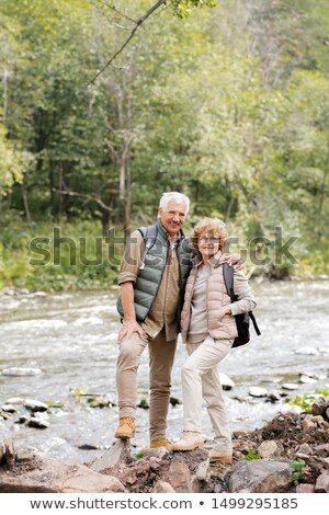 Stockfoto: Happy Aged Active Hikers With Backpacks Looking At You While Standing By River