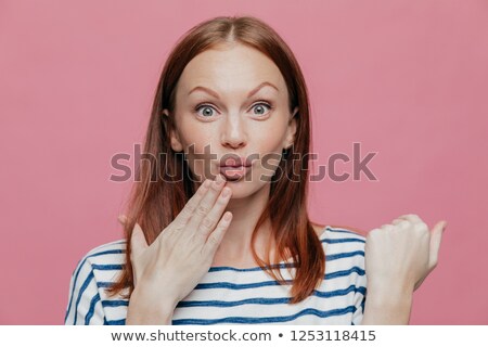 Stockfoto: Close Up Shot Of Attractive Woman Raises Eyebrows Pouts Lips Keeps Hand Near Mouth Has Brown Hair