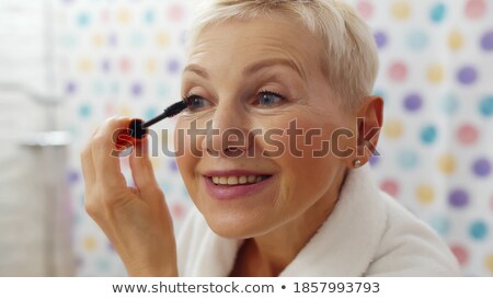 Foto d'archivio: Smiling Senior Woman With Mirror Applying Mascara