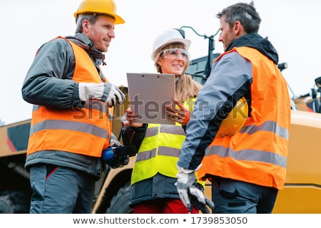 Foto d'archivio: Three Workers In A Quarry Discussing In Front Of Heavy Machinery