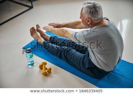 Сток-фото: Man Sitting Down On Exercise Mat While Touching His Toes