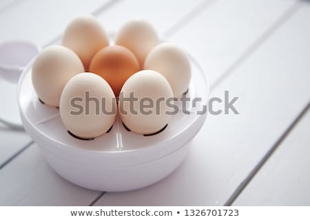 Foto stock: Chicken Eggs In A Egg Electric Cooker On A White Wooden Table