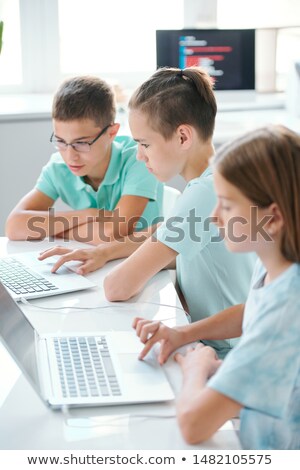 Row Of Serious Cute Schoolkids In Casualwear Sitting By Desk In Front Of Laptops Foto stock © Pressmaster