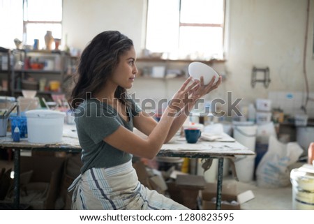 Stok fotoğraf: Serious Pretty Potter Examining Her Creation In The Pottery Workshop