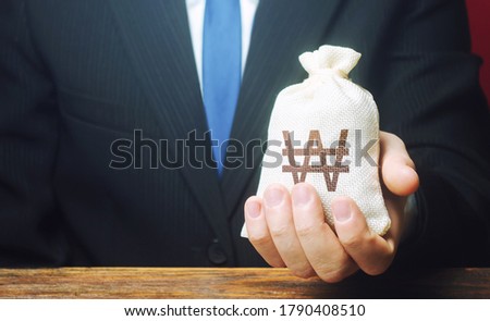 Stockfoto: A Businessman Holds In His Hand A South Korean Won Money Bag Stimulating Economic Recovery Investm