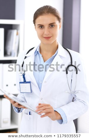 Stok fotoğraf: Female Doctor Pointing At Copy Space Holding Clipboard