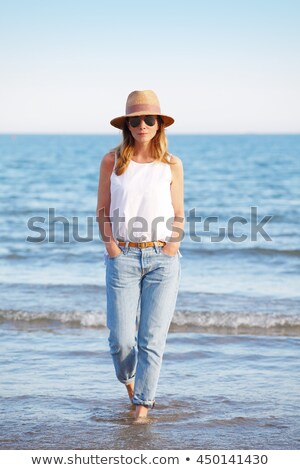 Stockfoto: Woman Walking Along Beach Wearing Straw Hat