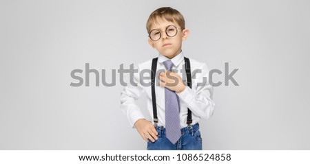 Foto stock: A Charming Boy In A White Shirt Suspenders A Tie And Light Jeans Stands On A Gray Background The