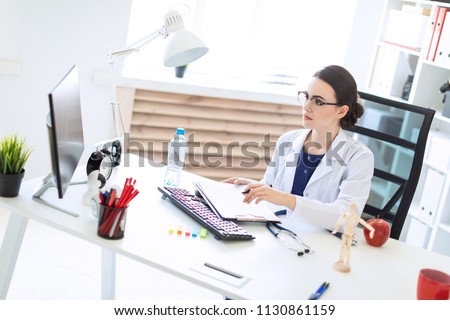 ストックフォト: A Young Girl In A White Robe Is Sitting At The Desk In The Office Talking On The Phone And Holding