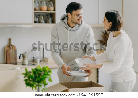 [[stock_photo]]: Delighted Housewife And Her Husband Unpack Cardboard Boxes With New Tableware Carry Plates Move In